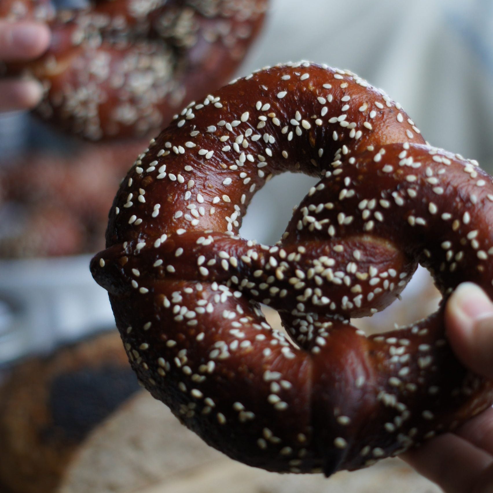 Two pretzels with sesame seeds held by a person, blurred background