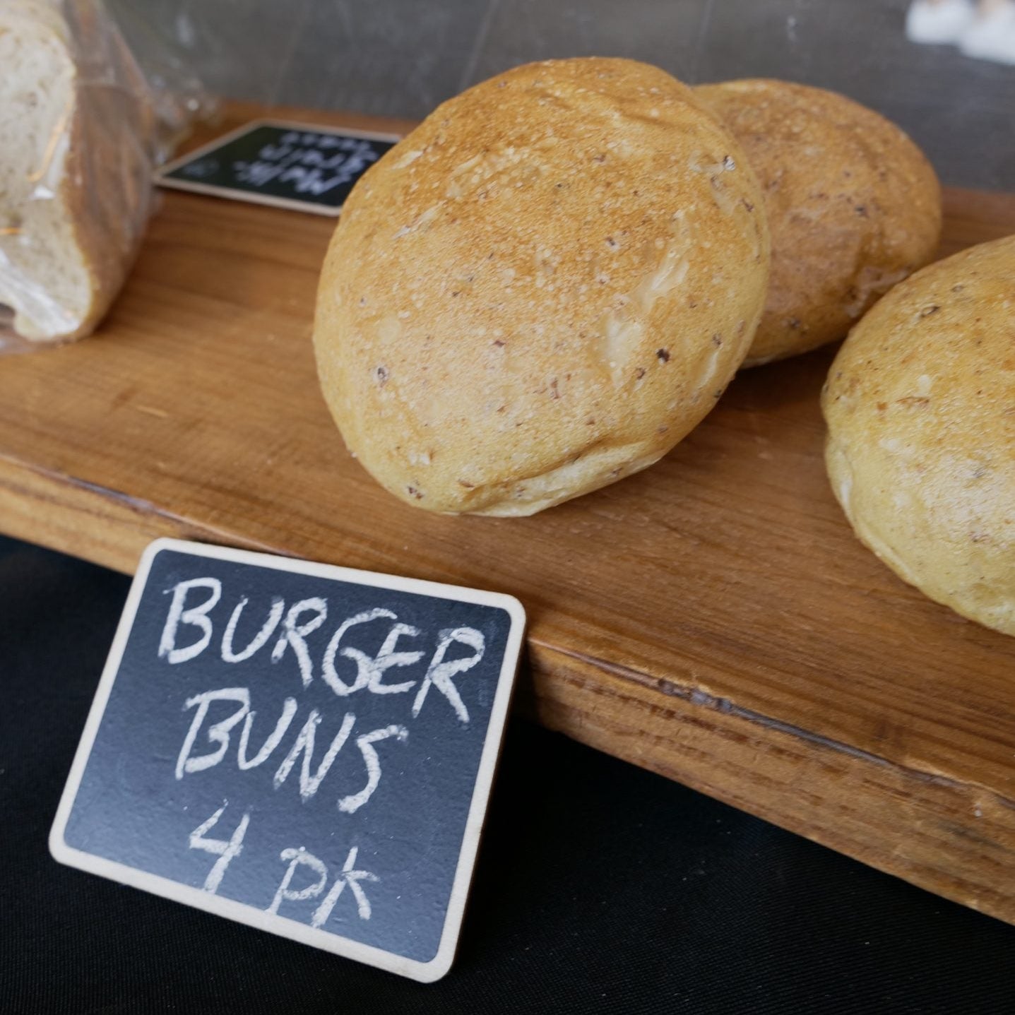 Burger buns on a wooden board with a sign indicating the quantity at an outdoor market.