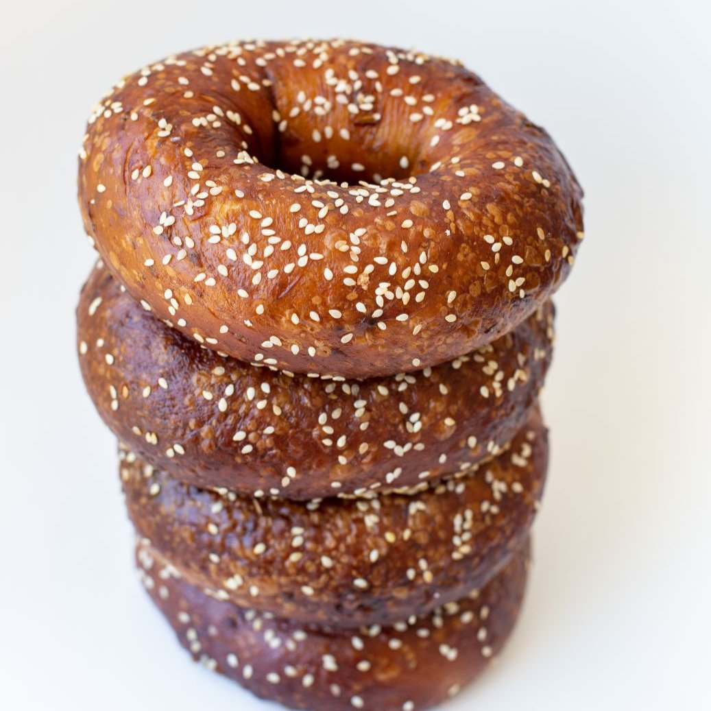 A stack of four pretzel bagels with visible sesame seeds sprinkled on the top crust.