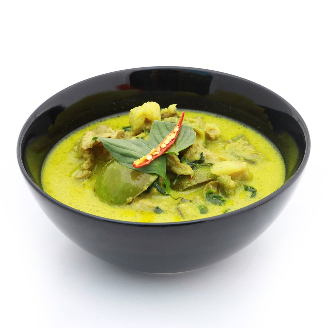 Bowl of Thai Green Curry Sauce with green peppers, basil leaves and a red chilli pepper.
